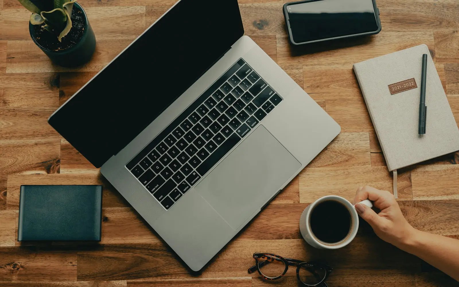 A desk with a laptop, notebook and coffee